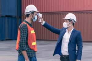 two employees wearing masks one taking the other temperature