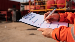 Action of safety office is writing on checklist paper during safety audit and risk verification at drilling site operation meeting OSHA requirements